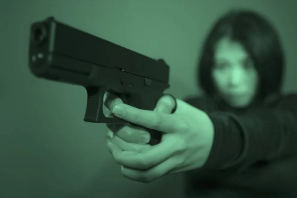 매력적 이고 위험해 보이는 젊은 여성 이 어두운 배경 과깊은 초점 이 있는 영화 스타일로 총을 들고 있는 극적 인 액션 사진 — 스톡 사진