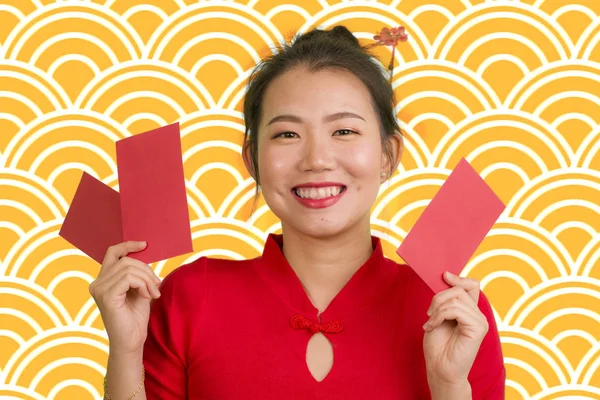 Jong gelukkig en mooi aziatische Chinese vrouw in traditionele Nieuwjaar rode jurk en haar broodje met rode zak enveloppen met geld als zegen van vrienden en familie — Stockfoto