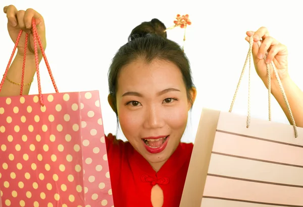 Feliz retrato de joven hermosa y emocionada mujer china asiática en vestido rojo sonriente emocionado sosteniendo bolsas alegre aislado sobre fondo blanco en concepto de moda — Foto de Stock