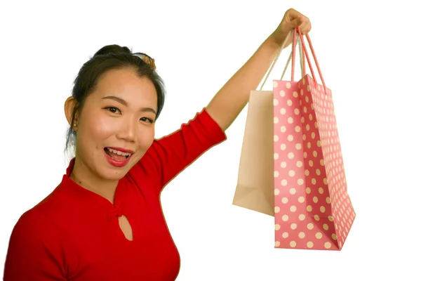 Feliz retrato de joven hermosa y emocionada mujer china asiática en vestido rojo sonriente emocionado sosteniendo bolsas alegre aislado sobre fondo blanco en concepto de moda — Foto de Stock