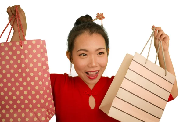 Feliz retrato de joven hermosa y emocionada mujer japonesa asiática en vestido rojo sonriente emocionado sosteniendo bolsas alegre aislado sobre fondo blanco en concepto de moda — Foto de Stock