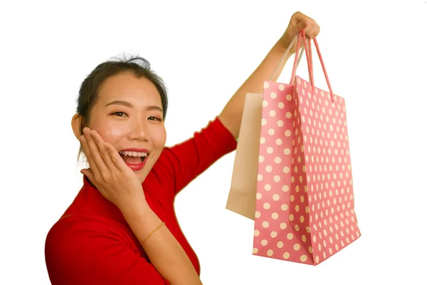 Kırmızı elbiseli güzel ve heyecanlı Asyalı kadının mutlu portresi. Elinde alışveriş torbalarıyla heyecanlı. Moda konseptinin beyaz arka planında neşeli bir şekilde izole edilmiş. — Stok fotoğraf