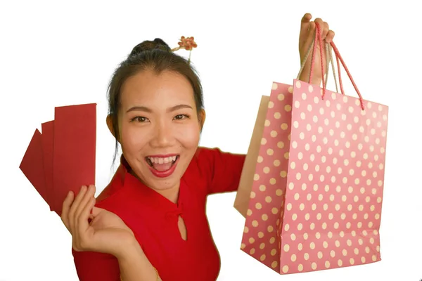 Mutlu ve güzel Asyalı, kırmızı elbiseli, neşeli gülümseyen, alışveriş torbaları taşıyan genç bir Çinli kadın Çin Yeni Yıl kırmızı cebine para girdikten sonra heyecanla para harcıyor. — Stok fotoğraf