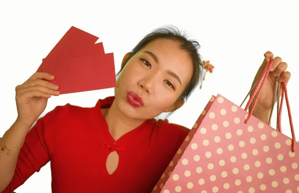 Młody szczęśliwy i piękny Azji chiński kobieta w czerwony strój uśmiechnięty wesoły trzymając torby na zakupy jako podekscytowany wydawanie pieniędzy po otrzymaniu chiński Nowy Rok czerwona kieszeń z pieniędzy — Zdjęcie stockowe