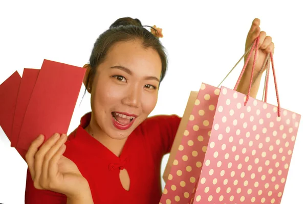Ung glad og smuk asiatisk koreansk kvinde i rød kjole smilende munter holder indkøbsposer så spændte lommepenge efter at have modtaget kinesisk nytår rød lomme med penge - Stock-foto