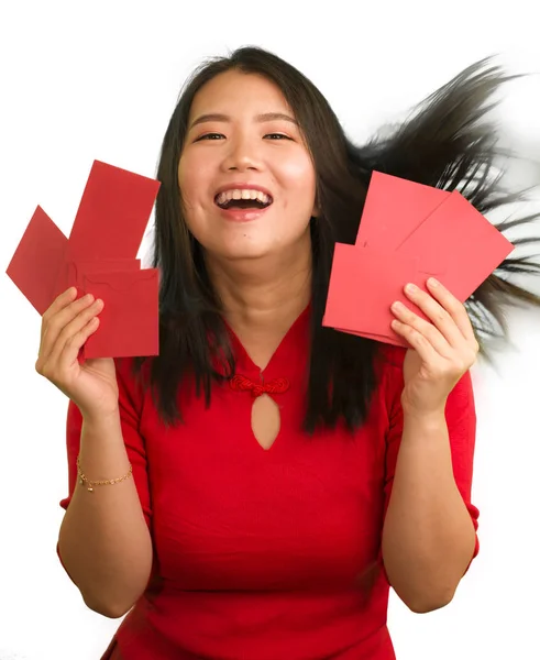 Νεαρή όμορφη και χαρούμενη Ασιάτισσα Κινέζα με παραδοσιακό κόκκινο φόρεμα και κουλούρι μαλλιών κρατώντας κόκκινους φακέλους τσέπης με χρήματα απολαμβάνοντας χαρούμενα την ευλογία — Φωτογραφία Αρχείου