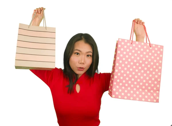 Młody szczęśliwy i piękny Azji chiński kobieta w czerwony strój uśmiechnięty wesoły gospodarstwa torby na zakupy jako podekscytowany zakupoholiczka dziewczyna izolowana na białym tle w koncepcji mody piękna — Zdjęcie stockowe