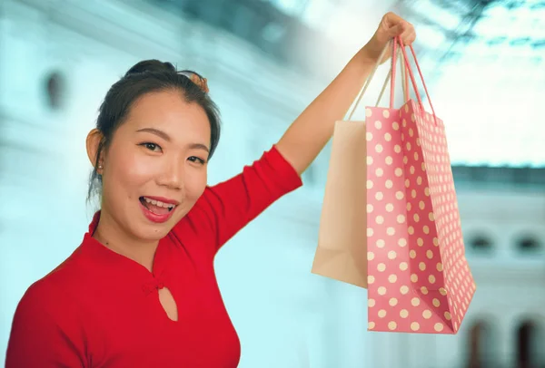 lifestyle portrait of young beautiful and happy Asian Korean woman holding shopping bags at modern shopping mall smiling excited and cheerful in shopaholic girl crazy about fashion