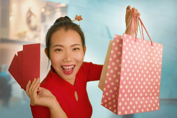 Lifestyle portrait of young beautiful and happy Asian Chinese woman holding Chinese New year red pockets and shopping bags at modern shopping mall smiling excited spending money — Stock Photo, Image