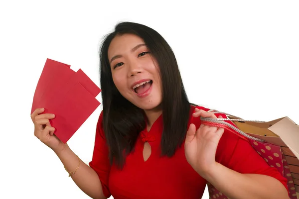 若いです幸せと美しいアジアの女性で赤いドレス笑顔陽気な保持ショッピングバッグとして興奮支出お金後中国の旧正月赤いポケットでお金を隔離 — ストック写真