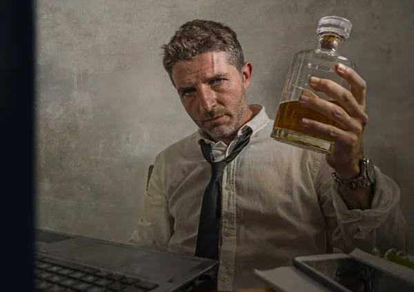 Алкогольний наркоман - драматичний портрет алкогольного чоловіка в втраті краватки, який п'є за офісним столом, працюючи марнотратно і безладно тримаючи пляшку віскі п'яною — стокове фото