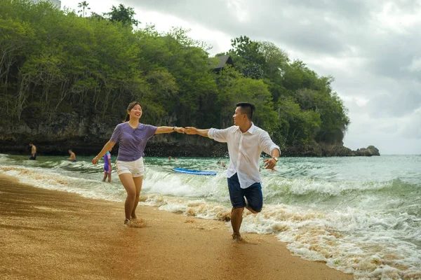 Summer holidays lifestyle portrait of young beautiful and sweet Asian Chinese couple in love running on the beach together enjoying honeymoon trip in the beach smiling cheerful — 스톡 사진