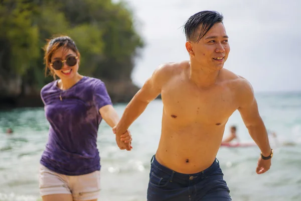 Летние каникулы образ жизни портрет молодой красивой и сладкой азиатской влюбленной пары, бегущей по пляжу вместе наслаждаясь поездкой медового месяца на пляже улыбаясь весело — стоковое фото