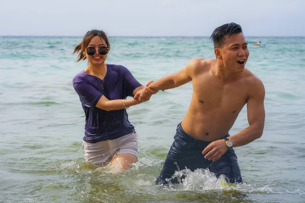 Summer holidays lifestyle portrait of young beautiful and sweet Asian Chinese couple in love running on the beach together enjoying honeymoon trip in the beach smiling cheerful — 스톡 사진