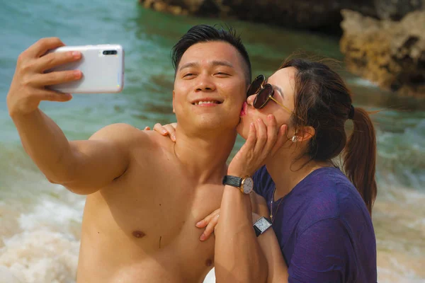 Férias de verão estilo de vida retrato de jovens felizes e brincalhão asiático casal turista chinês desfrutando na praia tirar foto selfie com telefone mão apreciando o mar juntos — Fotografia de Stock