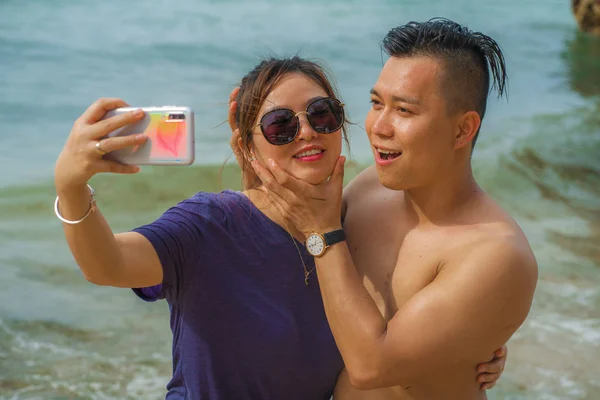 Férias de verão estilo de vida retrato de jovens felizes e brincalhão asiático casal turista chinês desfrutando na praia tirar foto selfie com telefone mão apreciando o mar juntos — Fotografia de Stock