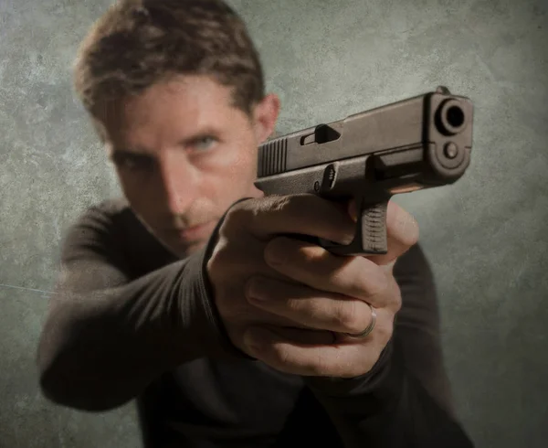 Grunge cinematic portrait of attractive and dangerous looking hitman or secret service especial agent man in action pointing gun in crime mob and criminal lifestyle concept — Stock Photo, Image