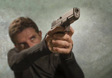 grunge cinematic portrait of attractive and dangerous looking hitman or secret service especial agent man in action pointing gun in crime mob and criminal lifestyle concept clipart