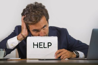 Depresyonda ve stresli takım elbiseli ve kravatlı çekici bir adam ezilmiş ofis bilgisayarında çalışıyor elinde not defteri tutarak hayal kırıklığına uğramış ve aşırı çalışılmış yardım istiyor.