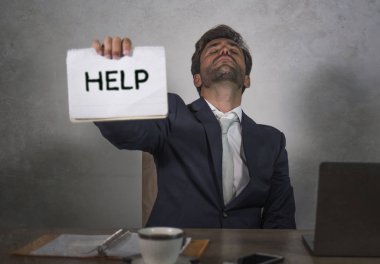 Depresyonda ve stresli takım elbiseli ve kravatlı çekici bir adam ezilmiş ofis bilgisayarında çalışıyor elinde not defteri tutarak hayal kırıklığına uğramış ve aşırı çalışılmış yardım istiyor.
