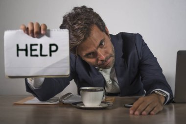 Depresyonda ve stresli takım elbiseli ve kravatlı çekici bir adam ezilmiş ofis bilgisayarında çalışıyor elinde not defteri tutarak hayal kırıklığına uğramış ve aşırı çalışılmış yardım istiyor.