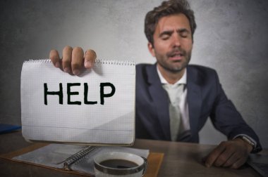 Depresyonda ve stresli takım elbiseli ve kravatlı çekici bir adam ezilmiş ofis bilgisayarında çalışıyor elinde not defteri tutarak hayal kırıklığına uğramış ve aşırı çalışılmış yardım istiyor.