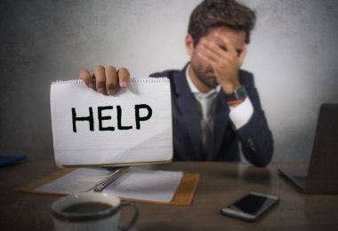 Depresyonda ve stresli takım elbiseli ve kravatlı çekici bir adam ezilmiş ofis bilgisayarında çalışıyor elinde not defteri tutarak hayal kırıklığına uğramış ve aşırı çalışılmış yardım istiyor.