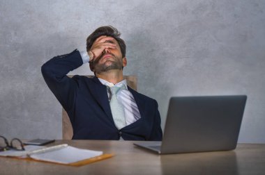Depresyonda ve stresli İspanyol takım elbiseli ve kravatlı çekici iş adamı ofis bilgisayarında çalışırken yorgun düşmüş ve başı dertte olan yönetici olarak çok çalışmış.