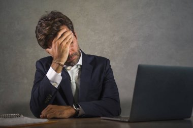 Depresyonda ve stresli İspanyol takım elbiseli ve kravatlı çekici iş adamı ofis bilgisayarında çalışırken yorgun düşmüş ve başı dertte olan yönetici olarak çok çalışmış.