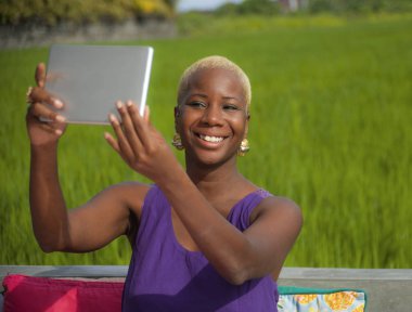 Çekici ve mutlu siyahi Afrikalı Amerikalı kadın havalı hipster tarzında özçekim yapıyor dışarıda dijital tabletle pirinç tarlasında yaz tatilinin tadını çıkarıyor.