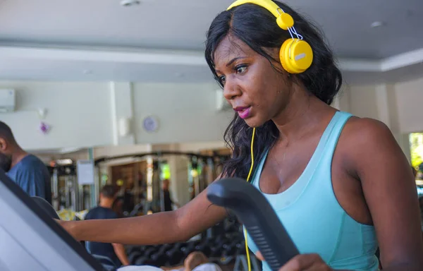 Estilo de vida de fitness retrato de la joven atractiva y feliz afro-americana negra entrenando en el gimnasio haciendo ejercicio de máquina elíptica escuchando música con auriculares — Foto de Stock