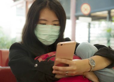 Korumalı yüz maskesi takarak havaalanında genç ve güzel bir turist olan Koreli kız Çin Coronavirüs salgınında internet haberlerini ve bilgileri cep telefonuyla kontrol ediyor. 