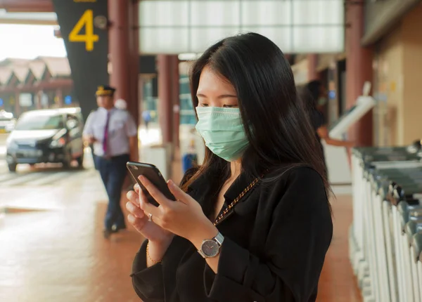 Юна красива жінка азіатського походження в аеропорту, одягнена в захисну маску, перевіряє інтернет-новини та інформацію мобільним телефоном на епідемії китайського коронавірусу — стокове фото