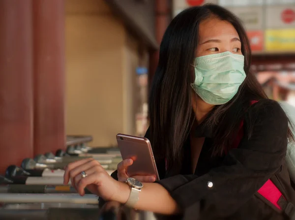 Young beautiful Asian Chinese student woman at airport wearing protective facial mask checking news and information with mobile phone on China Coronavirus epidemic outbreak — Stock Photo, Image