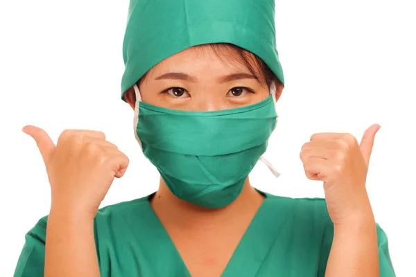 Young beautiful and happy Asian Chinese medicine doctor woman or hospital nurse in medical hat and scrub giving thumb up sign smiling cheerful behind surgeon face mask — 스톡 사진