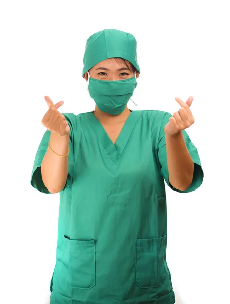 Молодая красивая и счастливая азиатка врач медицины или главная медсестра больницы в зеленых халатах и шляпе хирурга улыбаясь уверенно делая знак любви пальца — стоковое фото