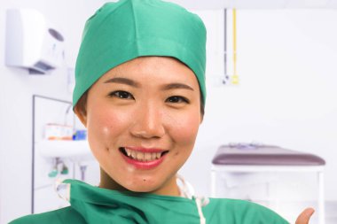 Genç, güzel ve mutlu Asyalı tıp doktoru ya da yeşil önlüklü hastane başhemşiresi ve sağlık hizmetleri konseptine güvenen bir cerrah şapkası.