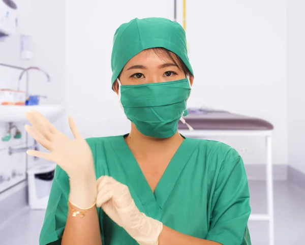 Young beautiful and happy Asian medicine doctor or chief hospital nurse in green scrubs and surgey hat and mask putting  latex gloves — 스톡 사진