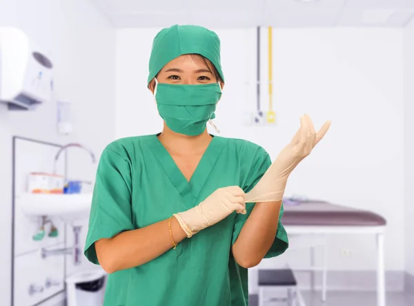 Young beautiful and happy Asian medicine doctor or chief hospital nurse in green scrubs and surgey hat and mask putting  latex gloves — 스톡 사진