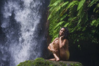 Açık havada, çekici ve mutlu hipster bir kadının, egzotik tatil beldelerindeki muhteşem şelalede özgür hissedişinin portresi.