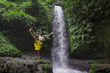 Genç çekici ve mutlu hippi kız dışarıda yoga yapıyor tropikal şelalede meditasyon yapıyor sağlıklı ve zen yaşam tarzında özgürlük ve doğanın tadını çıkarıyor.