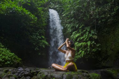 Genç çekici ve mutlu hippi kız dışarıda yoga yapıyor tropikal şelalede meditasyon yapıyor sağlıklı ve zen yaşam tarzında özgürlük ve doğanın tadını çıkarıyor.