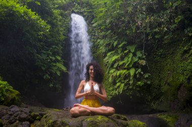 Genç çekici ve mutlu hippi kız dışarıda yoga yapıyor tropikal şelalede meditasyon yapıyor sağlıklı ve zen yaşam tarzında özgürlük ve doğanın tadını çıkarıyor.