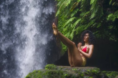Genç çekici ve mutlu hippi kız dışarıda yoga yapıyor tropikal şelalede meditasyon yapıyor sağlıklı ve zen yaşam tarzında özgürlük ve doğanın tadını çıkarıyor.