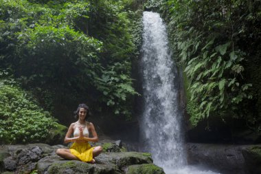 Genç çekici ve mutlu hippi kadın dışarıda yoga yapıyor tropikal şelalede meditasyon yapıyor sağlıklı ve zen yaşam tarzında özgürlük ve doğanın tadını çıkarıyor.
