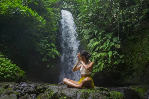 Jovem mulher hipster atraente e feliz fazendo ioga ao ar livre na bela cachoeira tropical meditando desfrutando de liberdade e natureza em estilo de vida saudável e zen — Fotografia de Stock