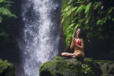 Açık havada, çekici ve mutlu hipster bir kadının, egzotik tatil beldelerindeki muhteşem şelalede özgür hissedişinin portresi.