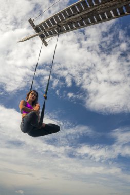 Aero yoga egzersizi - genç çekici ve atletik kadın hava yogası alıştırması yapıyor akrobatik vücut duruşlarını dengeli bir şekilde mavi gökyüzünde izole ediyor. 