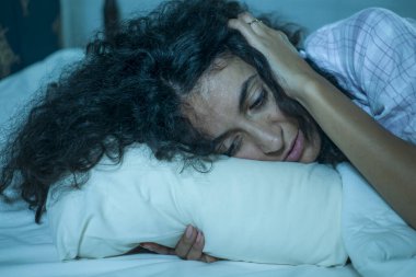 Genç üzgün ve bunalımlı kıvırcık saçlı, yatakta uykusuz, düşünceli, depresyon sorunu ve uykusuzluk sorunu yaşayan bir kadın.