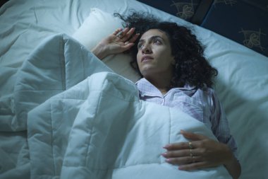 Genç üzgün ve bunalımlı kıvırcık saçlı, yatakta uykusuz, düşünceli, depresyon sorunu ve uykusuzluk sorunu yaşayan bir kadın.